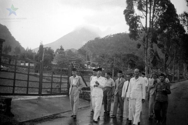 Group of men in light-colored suits and traditional caps walking along a wet road beside a wooden fence, with hills/volcano in the background.