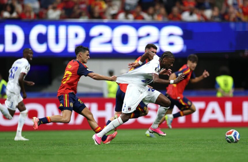 Soccer players chase the ball in a crowded stadium, a player in red and gold pulls on another player's white kit.