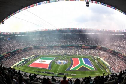 Bird's-eye view of a full stadium with a circular field display featuring large national flags and cheering spectators.