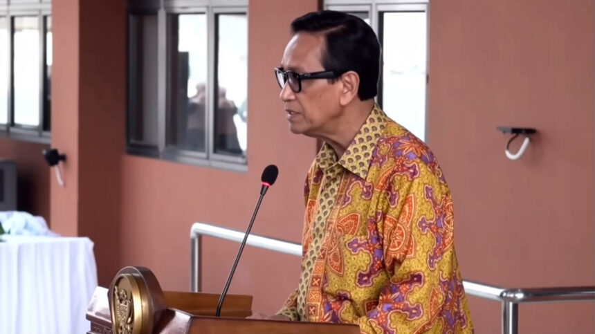 Man in a patterned shirt speaks at a podium with a microphone in a conference setting.