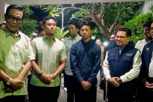 Group of men in smart casual and jackets posing for a photo in a hallway with greenery in the background, forming a formal line up.