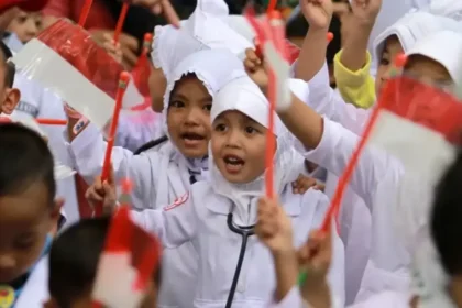 A group of children in white uniforms waving red flags, celebrating together at a crowd event.