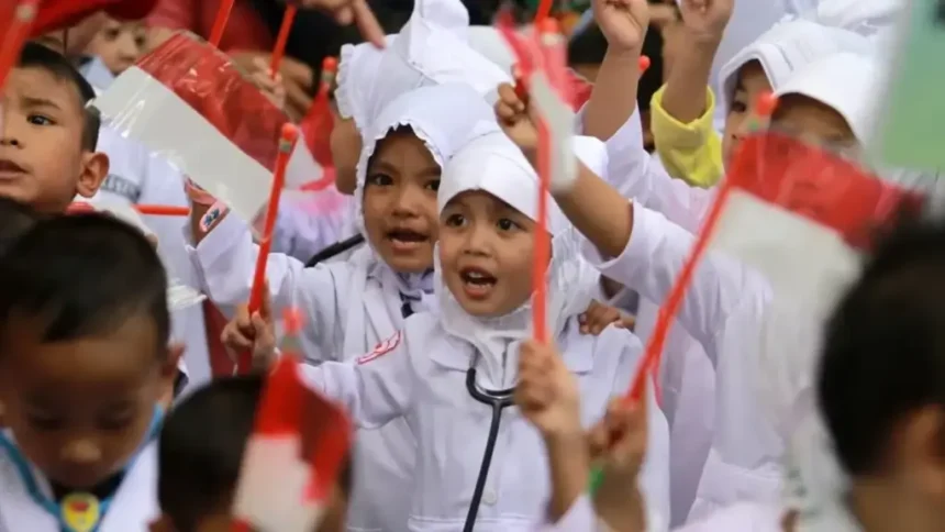 A group of children in white uniforms waving red flags, celebrating together at a crowd event.