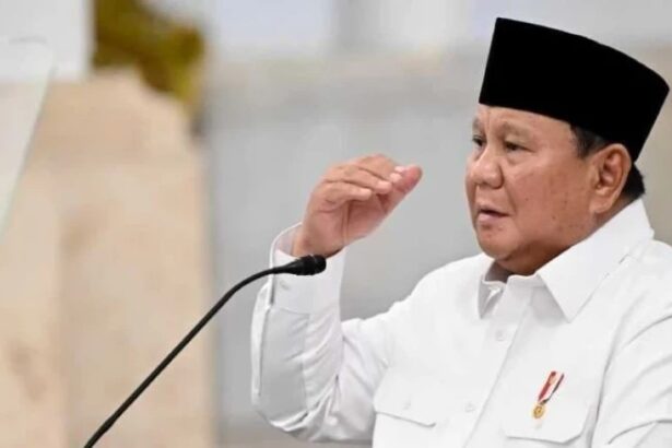 Man wearing a white shirt and black cap speaking into a microphone at a podium.