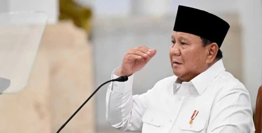 Man wearing a white shirt and black cap speaking into a microphone at a podium.