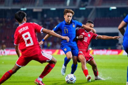 Soccer players in blue and red uniforms contest the ball on a green pitch during a match.