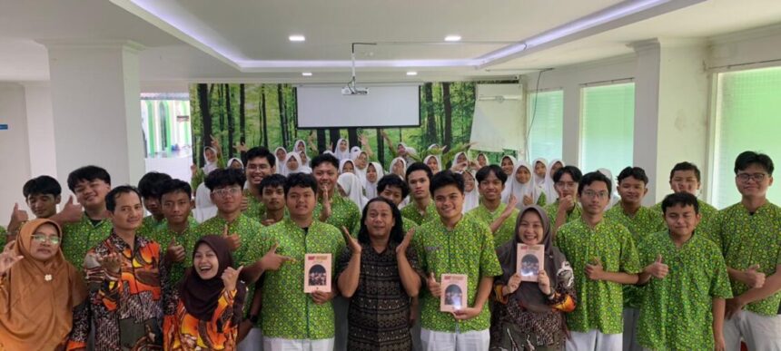 Tedi MAN 1 Yk - Mabur.co Group of students in matching green shirts posing for a photo in a classroom, two adults in front holding books/destinations, forest mural in the background.