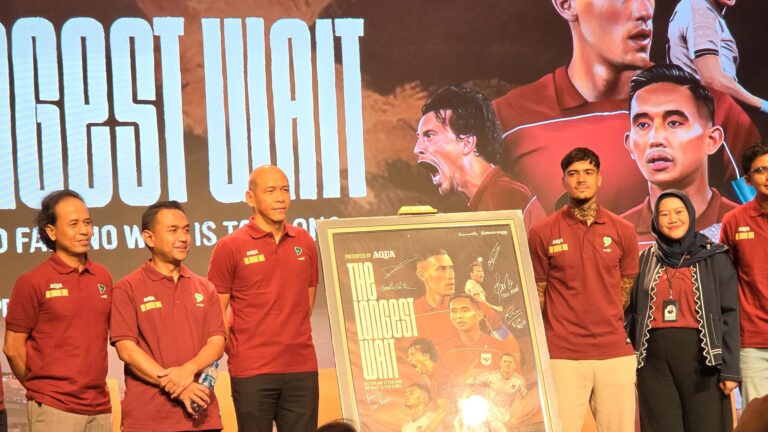 Group of people in maroon polo shirts standing on a stage with a framed poster board featuring signed photos of athletes.