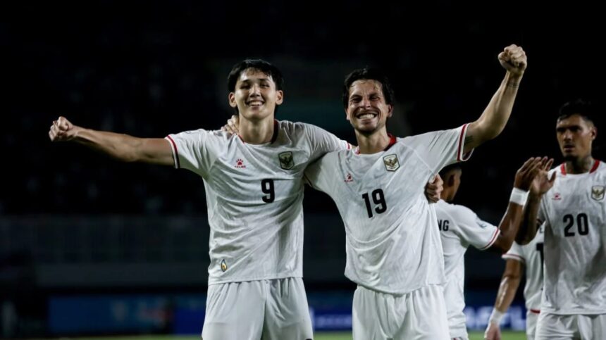 Two soccer players in white jerseys (numbers 9 and 19) celebrate with arms around each other on a night field, smiles on their faces.
