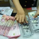 Hands counting a mixed stack of yuan and US dollar bills on a counter.