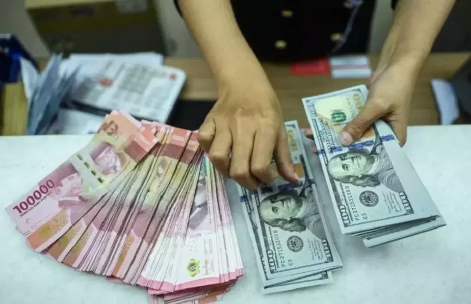 Hands counting a mixed stack of yuan and US dollar bills on a counter.