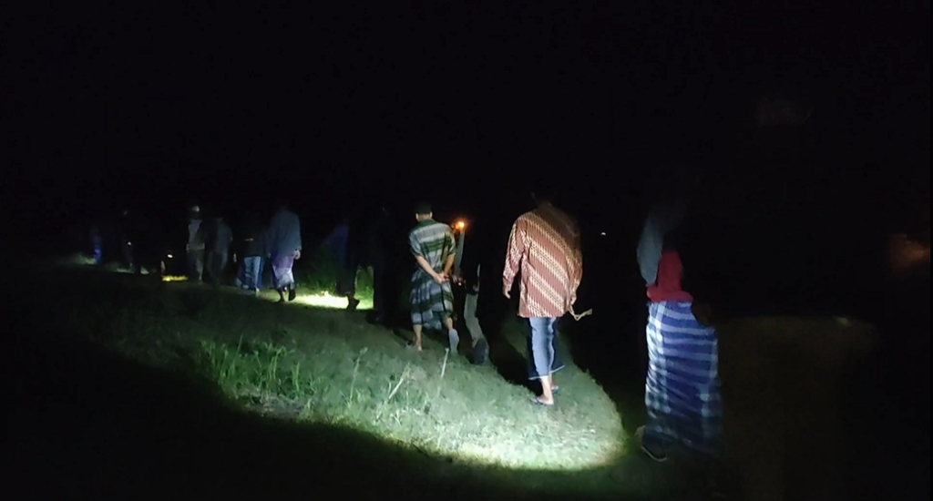Untitle3d - Mabur.co Line of people walking single file along a grassy path at night, lit by a distant flashlight beam on the ground