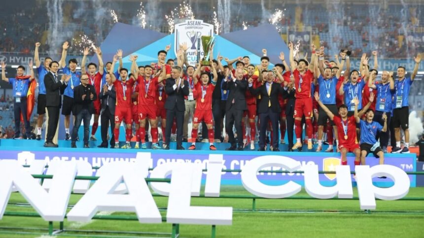 Soccer team in red uniforms celebrates on stage after winning, raising arms with the trophy as fireworks light the stadium.
