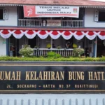 Front facade of Bung Hatta Birth House with red-white bunting and a large black-and-gold sign reading 'RUMAH KELAHIRAN BUNG HATTA' at No. 37, Bukittinggi