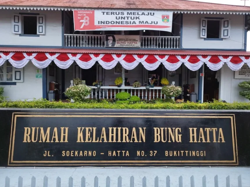 Front facade of Bung Hatta Birth House with red-white bunting and a large black-and-gold sign reading 'RUMAH KELAHIRAN BUNG HATTA' at No. 37, Bukittinggi