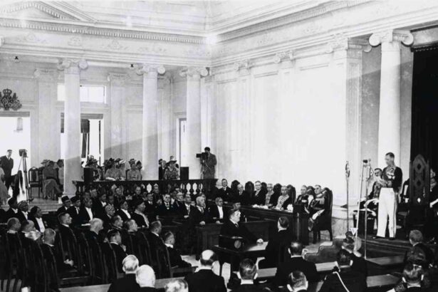Black-and-white photo of a formal parliamentary session in a columned hall, delegates seated and a speaker at a podium.