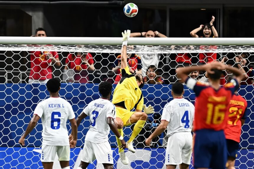 Soccer goalkeeper in yellow leaps to save ball at the goal as white-team players watch in front of the net.