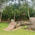 Outdoor garden with several large abstract stone sculptures on a green lawn, backed by trees and shrubbery.