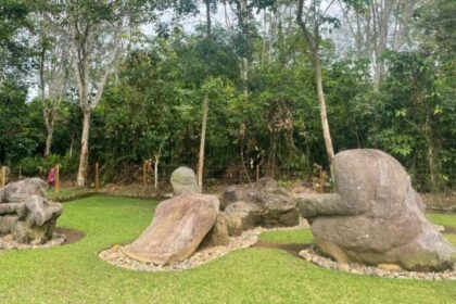 Outdoor garden with several large abstract stone sculptures on a green lawn, backed by trees and shrubbery.