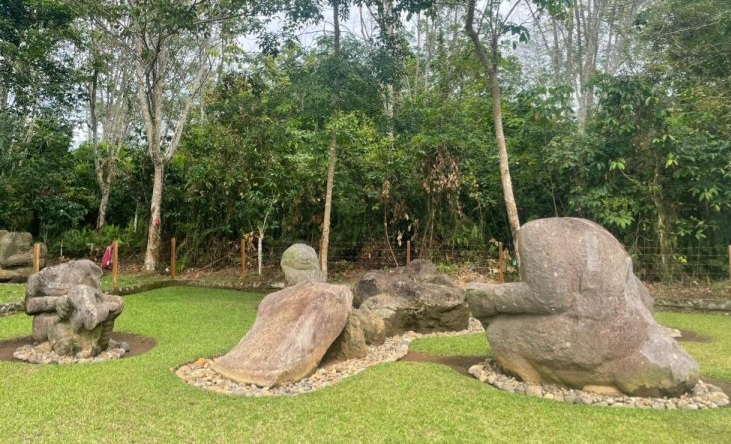 Outdoor garden with several large abstract stone sculptures on a green lawn, backed by trees and shrubbery.