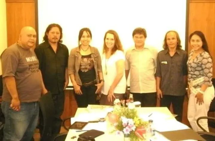 Eight adults stand side by side behind a conference table with papers and a floral centerpiece, posing for a group photo in a meeting room.