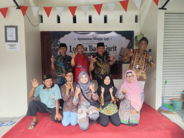 Group of Indonesian adults posing for a community photo in front of a banner reading 'Komunitas Minggu Legi', all thumbs-up and smiling under red-and-white bunting.