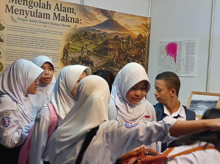 Group of Indonesian female students in white hijab uniforms gathered around a museum display featuring a volcano painting and informational panels.