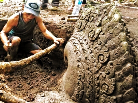 WhatsApp Image 2026-05-08 at 22.41.15 - Mabur.co Person kneeling in mud, digging around a large ornate carved stone wheel.