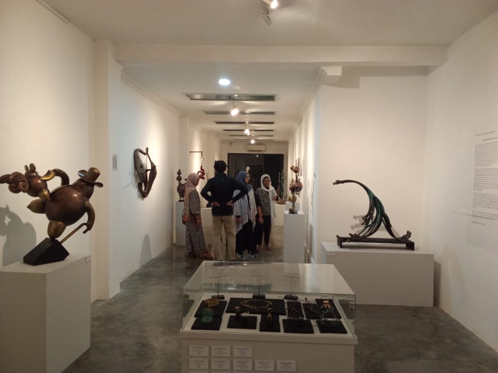 Group of visitors in a bright contemporary art gallery viewing abstract sculptures on plinths and display cases.