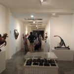 Group of visitors in a bright contemporary art gallery viewing abstract sculptures on plinths and display cases.