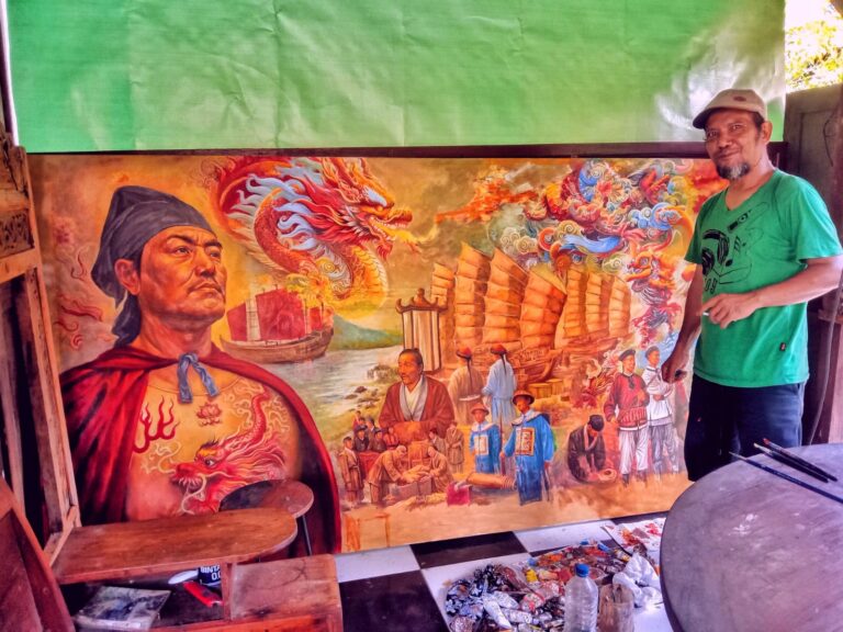 Man in a green shirt and cap stands beside a large, colorful mural featuring a dragon, ships, and people by the waterfront.