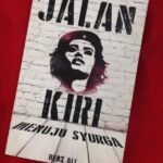 Stencil-style poster featuring a woman's portrait on a white brick background, tilted on a red surface; large text at top says 'JALAN KIRI' with additional text below.