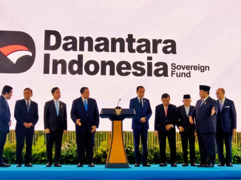 Group of officials in suits on a blue stage with a podium, in front of a Danantara Indonesia Sovereign Fund backdrop logo.