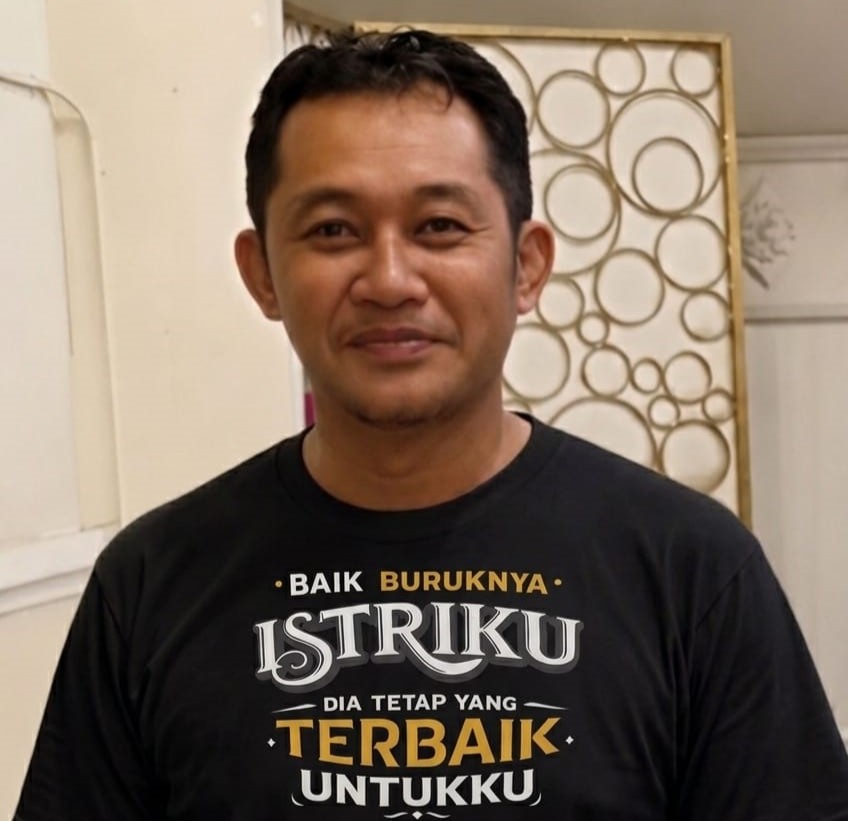 Smiling man in a black T-shirt with Indonesian text:'BAIK BURUKNYA ISTRIKU DIA TETAP YANG TERBAIK UNTUKKU'