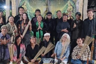 Group of adults posing for a group photo at a cultural ceremony, several holding palm fronds, with ritual food offerings arranged in front.