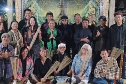 Group of adults posing for a group photo at a cultural ceremony, several holding palm fronds, with ritual food offerings arranged in front.