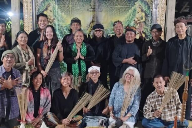 Group of adults posing for a group photo at a cultural ceremony, several holding palm fronds, with ritual food offerings arranged in front.