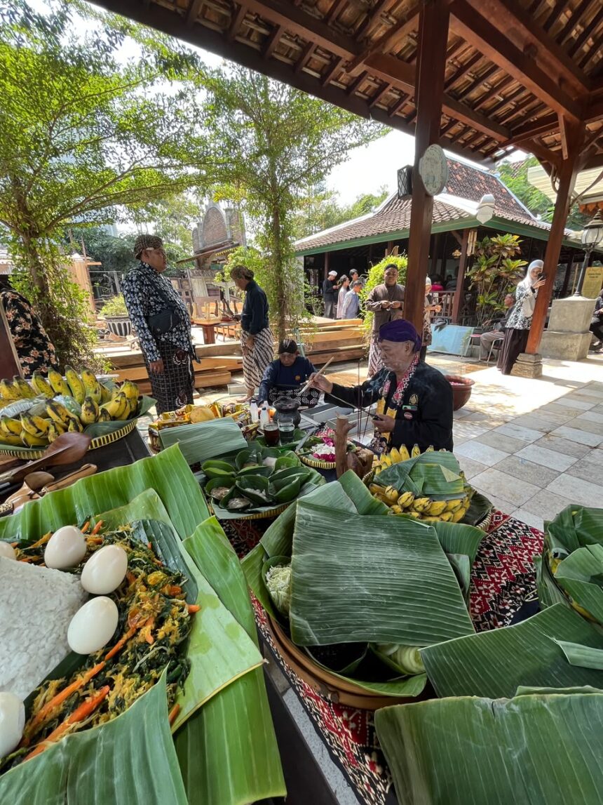 Market scene with banana leaf platters of food, eggs, bananas, and vegetables as people in traditional clothing browse under a wooden pavilion.