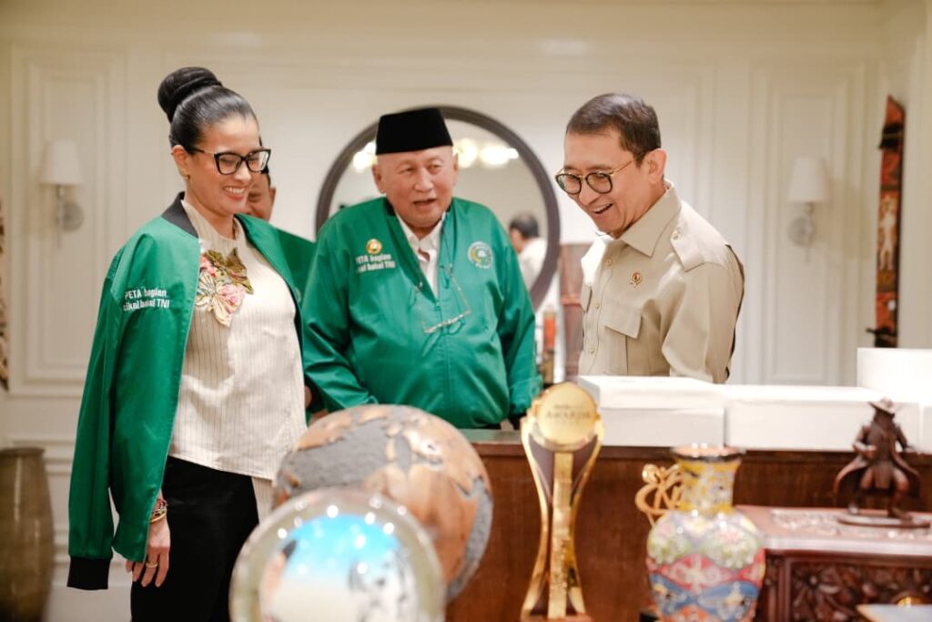 WhatsApp Image 2026-07-30 at 105100 - Mabur.co Three people smile and look at a globe and decorative trophies on a display table in a bright, formal room.