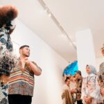 Group of people in batik clothing admiring an art installation in a gallery, bright white walls behind them.