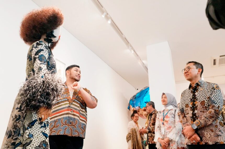 Group of people in batik clothing admiring an art installation in a gallery, bright white walls behind them.