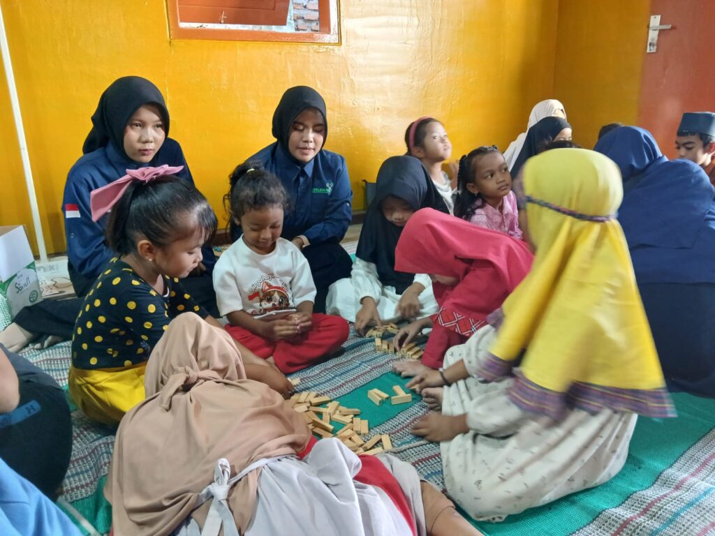 Group of children and women on a colorful mat inside a yellow-walled room, building with wooden blocks.