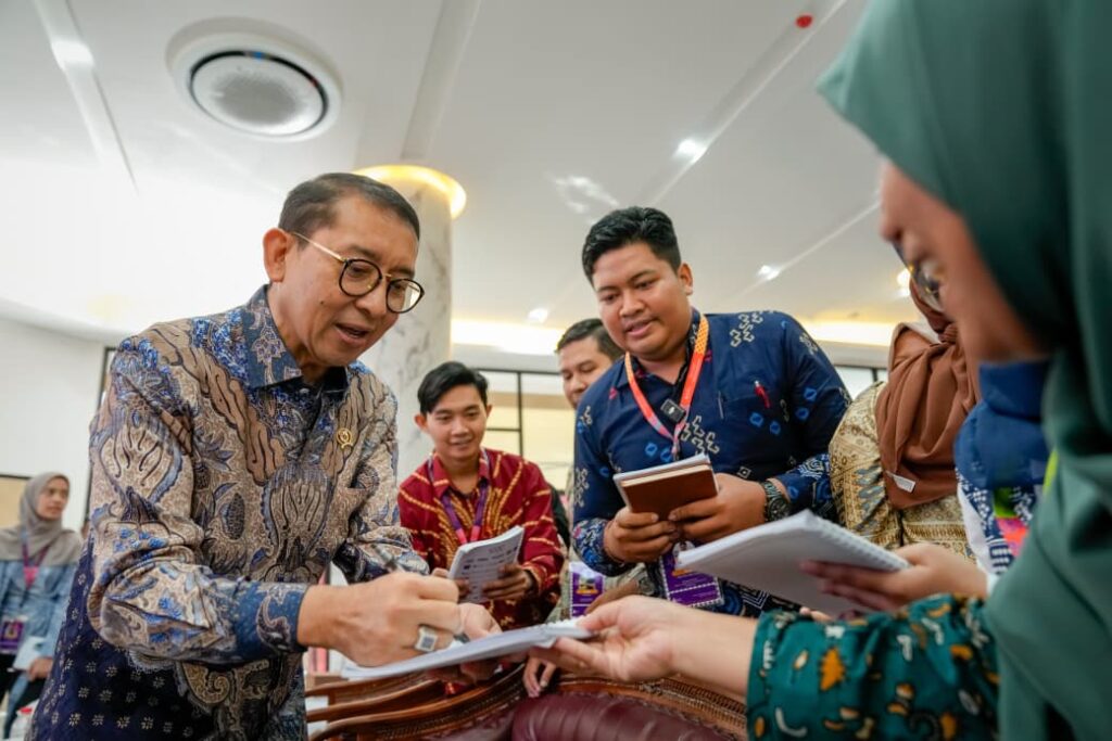 WhatsApp Image 2026-08-14 at 105243 - Mabur.co Man in a patterned shirt signs a document while colleagues hold papers and notebooks around him.