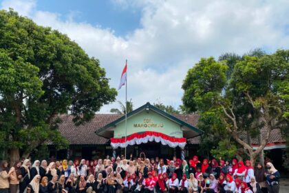 Large group of students and teachers posing for a photo in front of SDN Margorejo school, with an Indonesian flag and red-white bunting overhead.