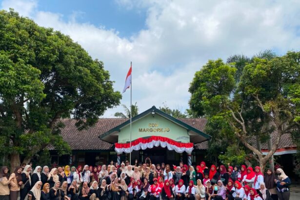 Large group of students and teachers posing for a photo in front of SDN Margorejo school, with an Indonesian flag and red-white bunting overhead.