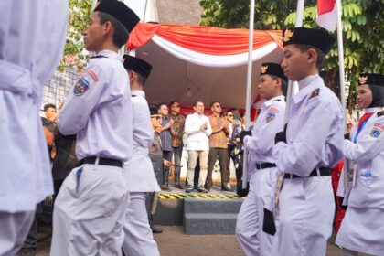 Group of cadets in white uniforms marching past a crowd under a red-and-white tent backdrop.