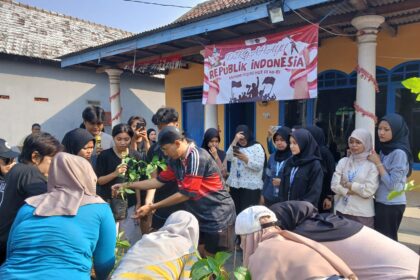 Crowd of people, many in hijabs, planting young saplings together at an outdoor Indonesia Independence Day event with a banner in the background.