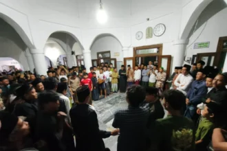 Large crowd of men and boys forming a circle in a white arched hall during a community gathering, center of attention unclear