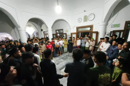 Large crowd of men and boys forming a circle in a white arched hall during a community gathering, center of attention unclear