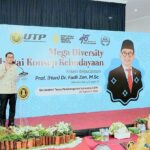 Speaker at a podium on a stage with a blue banner reading 'Mega Diversity' during a cultural event at Universitas Tunas Pembangunan Surakarta (UTP Surakarta).